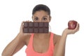 Young attractive hispanic woman in fitness top holding apple fruit and chocolate bar in her hands Royalty Free Stock Photo
