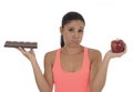 Young attractive hispanic woman in fitness top holding apple fruit and chocolate bar in her hands Royalty Free Stock Photo