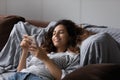 Young attractive Hispanic woman resting on sofa with smartphone Royalty Free Stock Photo