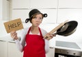 Young attractive home cook woman in red apron at kitchen holding pan and household with pot on her head in stress Royalty Free Stock Photo