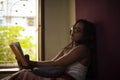 Young Indian brunette woman in white sleeping wear reading book on a bed Royalty Free Stock Photo