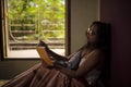 Young Indian brunette woman in white sleeping wear reading book on a bed Royalty Free Stock Photo