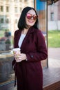 Young attractive lady in marsala coat drink coffee to go. Smiling beautiful hipster happy woman in city street, wearing Royalty Free Stock Photo