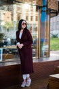 Young attractive lady in marsala coat drink coffee to go. Smiling beautiful hipster happy woman in city street, wearing Royalty Free Stock Photo