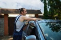Young attractive Latin American man in blue overalls, manually washing his car outdoors with cleaning foam and sponge. Royalty Free Stock Photo