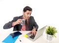 Young attractive Latin businessman in suit and tie working at office computer desk drinking cup of coffee Royalty Free Stock Photo