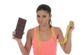 Young attractive latin woman holding taylor measure tape and chocolate bar in healthy nutrition diet Royalty Free Stock Photo