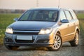 Young attractive long-haired woman inside shiny silver car at steering wheel on gravel empty road on bright blurred summer sunny