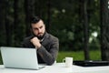 Young attractive male businessman in brown suit and tie sits at desk and works on computer outdoors. Green trees, nature Royalty Free Stock Photo