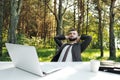 Young attractive male businessman in suit sitting at desk in forest of nature park. Stretches and rests from work. Royalty Free Stock Photo