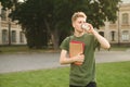 Young attractive male student holding notebooks and drinking take away coffee near the university. Handsome college student in the