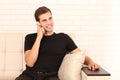 Young attractive man in black shirt is sitting on the sofa and talking on phone at home. Copy space Royalty Free Stock Photo