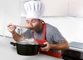 Young attractive man in chef hat and red cook apron testing flavor Royalty Free Stock Photo