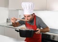 Young attractive man in chef hat and red cook apron testing flavor Royalty Free Stock Photo