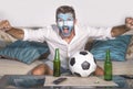 Young attractive man football supporter with Argentina flag painted face happy and excited watching cup match on TV celebrating vi Royalty Free Stock Photo