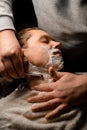 Young attractive man getting shave by barber while sitting in chair at barbershop