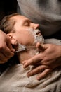 Young attractive man getting shave by male barber while sitting in chair at modern barbershop