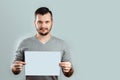 A young, attractive man holding a blank white A4 sheet, on a light background. mockup, layout, copy space