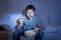 Young attractive man at home lying on couch watching tv holding popcorn bowl eating Royalty Free Stock Photo