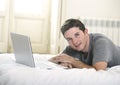 Young attractive man lying on bed or couch enjoying social networking using computer laptop at home Royalty Free Stock Photo