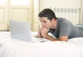 Young attractive man lying on bed or couch enjoying social networking using computer laptop at home Royalty Free Stock Photo