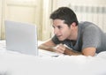 Young attractive man lying on bed or couch enjoying social networking using computer laptop at home Royalty Free Stock Photo