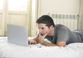 Young attractive man lying on bed or couch enjoying social networking using computer laptop at home wireless internet Royalty Free Stock Photo