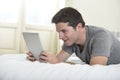 Young attractive man lying on bed or couch enjoying social networking using digital tablet computer internet at home Royalty Free Stock Photo