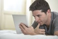 Young attractive man lying on bed or couch enjoying social networking using digital tablet computer internet at home Royalty Free Stock Photo