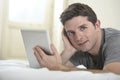 Young attractive man lying on bed or couch enjoying social networking using digital tablet computer internet at home Royalty Free Stock Photo