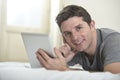 Young attractive man lying on bed or couch enjoying social networking using digital tablet computer internet at home Royalty Free Stock Photo