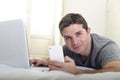 Young attractive man lying on bed or couch using mobile phone and computer laptop internet addict Royalty Free Stock Photo