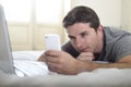 Young attractive man lying on bed or couch using mobile phone and computer laptop internet addict Royalty Free Stock Photo