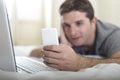 Young attractive man lying on bed or couch using mobile phone and computer laptop internet addict Royalty Free Stock Photo