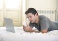 Young attractive man lying on bed or couch using mobile phone and computer laptop working from home Royalty Free Stock Photo