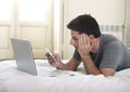 Young attractive man lying on bed or couch using mobile phone and computer laptop working from home Royalty Free Stock Photo