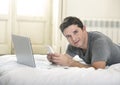 Young attractive man lying on bed or couch using mobile phone and computer laptop working from home Royalty Free Stock Photo