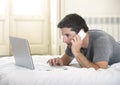 Young attractive man lying on bed or couch using mobile phone and computer laptop working from home Royalty Free Stock Photo