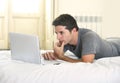 Young attractive man lying on bed or couch working on computer laptop typing connected to internet Royalty Free Stock Photo