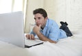 Young attractive man lying on bed enjoying social networking using computer at home Royalty Free Stock Photo