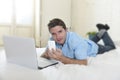 Young attractive man lying on bed using mobile phone and computer laptop working from home Royalty Free Stock Photo