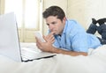 Young attractive man lying on bed using mobile phone and laptop working from home Royalty Free Stock Photo