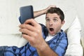 Young attractive man lying at home couch using internet on mobile phone looking surprised and shocked