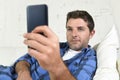 Young attractive man lying relaxed at home couch texting and surfing on internet in his mobile phone Royalty Free Stock Photo