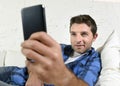 Young attractive man lying relaxed at home couch texting and surfing on internet in his mobile phone Royalty Free Stock Photo