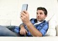 Young attractive man lying relaxed at home couch texting and surfing on internet in his mobile phone Royalty Free Stock Photo