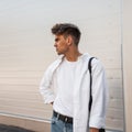 Young attractive man model in an elegant white shirt in a T-shirt in blue stylish jeans with a vintage bag stands on the street Royalty Free Stock Photo