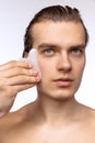 Young attractive man with perfect smooth skin, applying face massagers isolated over white studio background. Cosmetics