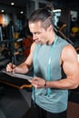 young attractive man personal trainer planning workout with clipboard in gym Royalty Free Stock Photo