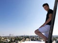 Young attractive man posing in front of camera on the roof of a residential building standing on a ladder